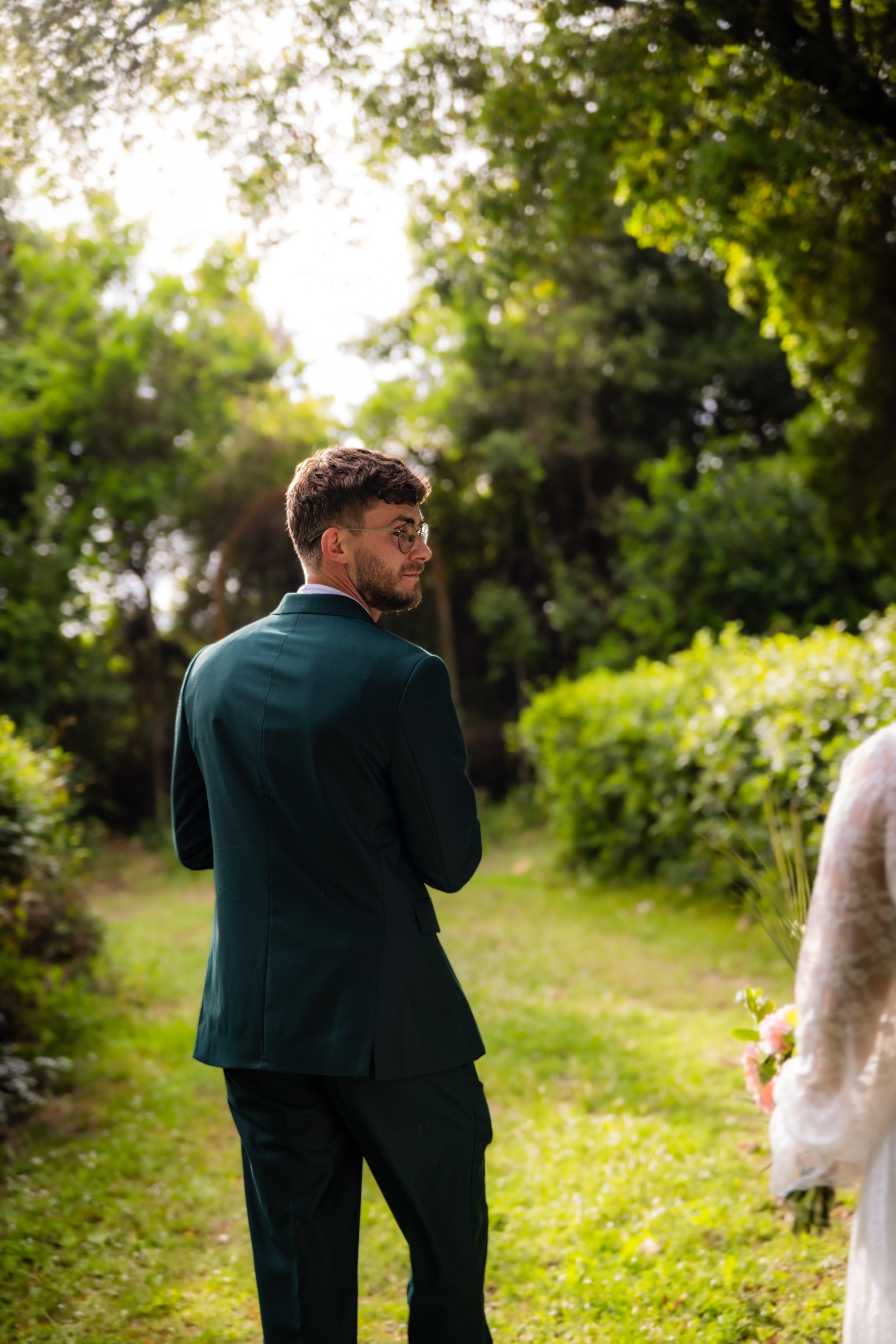 Le marié, de dos, dans le jardin, la mariée à ses côtés